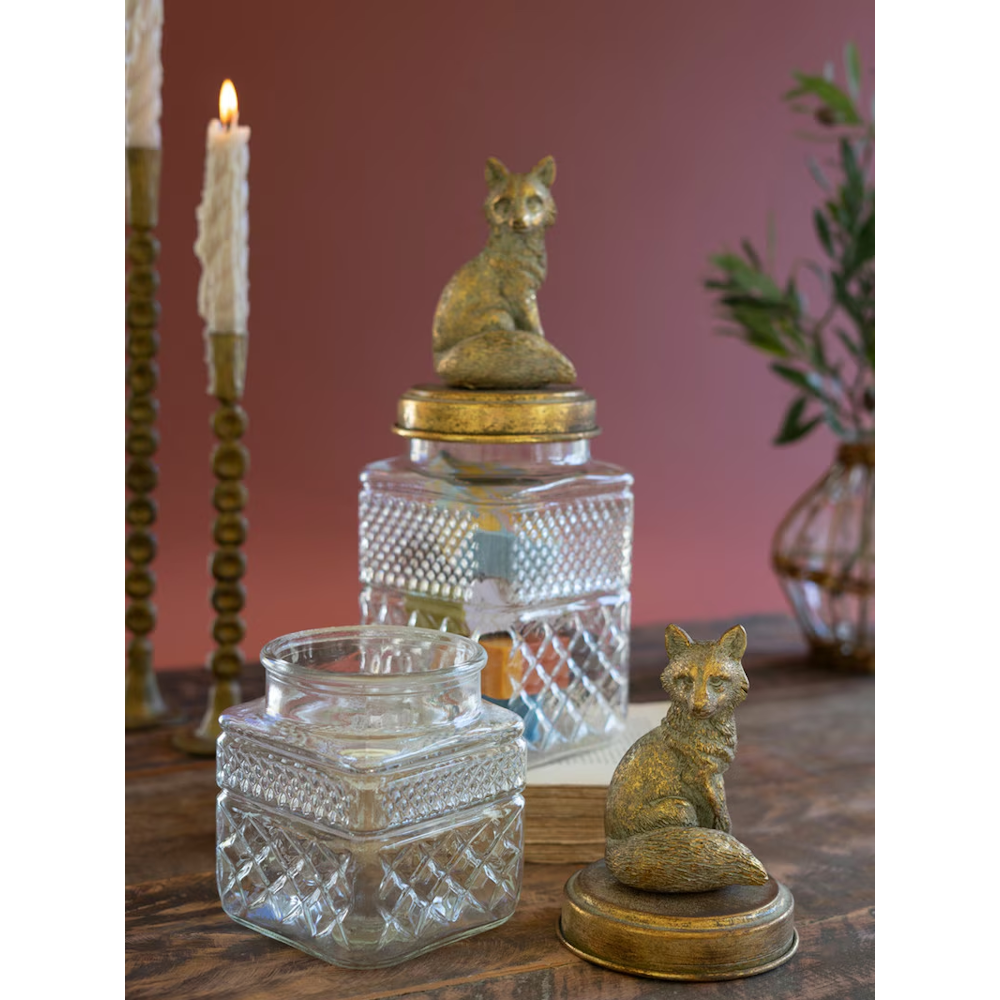 Textured glass canisters shown with one brass fox lid removed, set beside a burning candle.