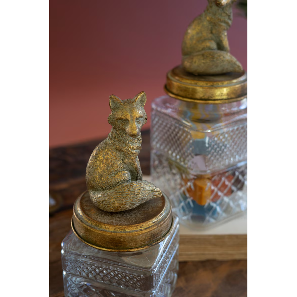 Close-up of textured glass canisters with brass fox lids displayed on a wooden surface.