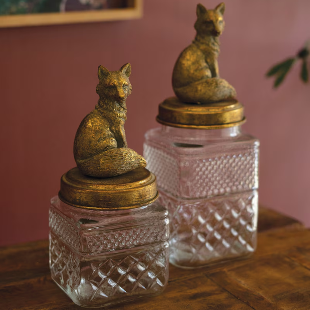 Two clear glass canisters with textured diamond patterns topped with brass-colored fox figurines.