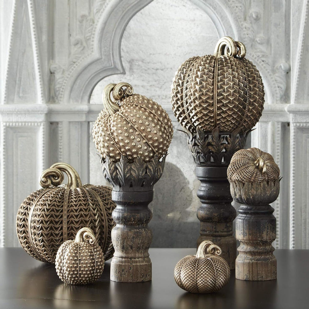 Textured antique gold decorative pumpkins displayed on rustic pedestals against a stone wall.