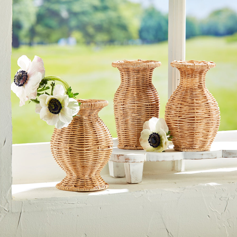 Three resin basket-weave vases with white anemone flowers on a sunny windowsill overlooking a green field.