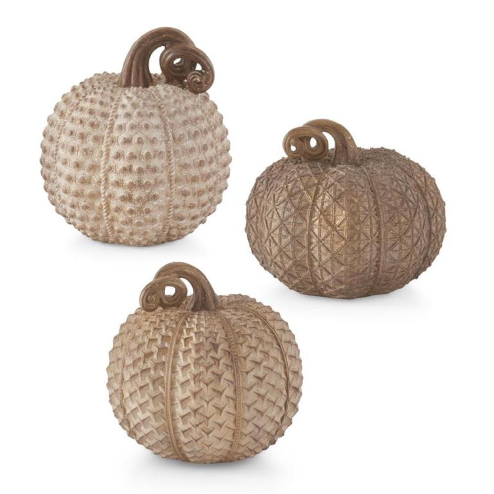 Three beige decorative resin pumpkins with distinct geometric textures and curled brown stems.