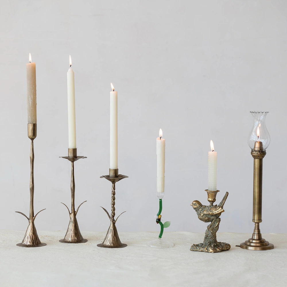 Collection of antique gold and vintage style taper candle holders with lit white candles on a neutral background.