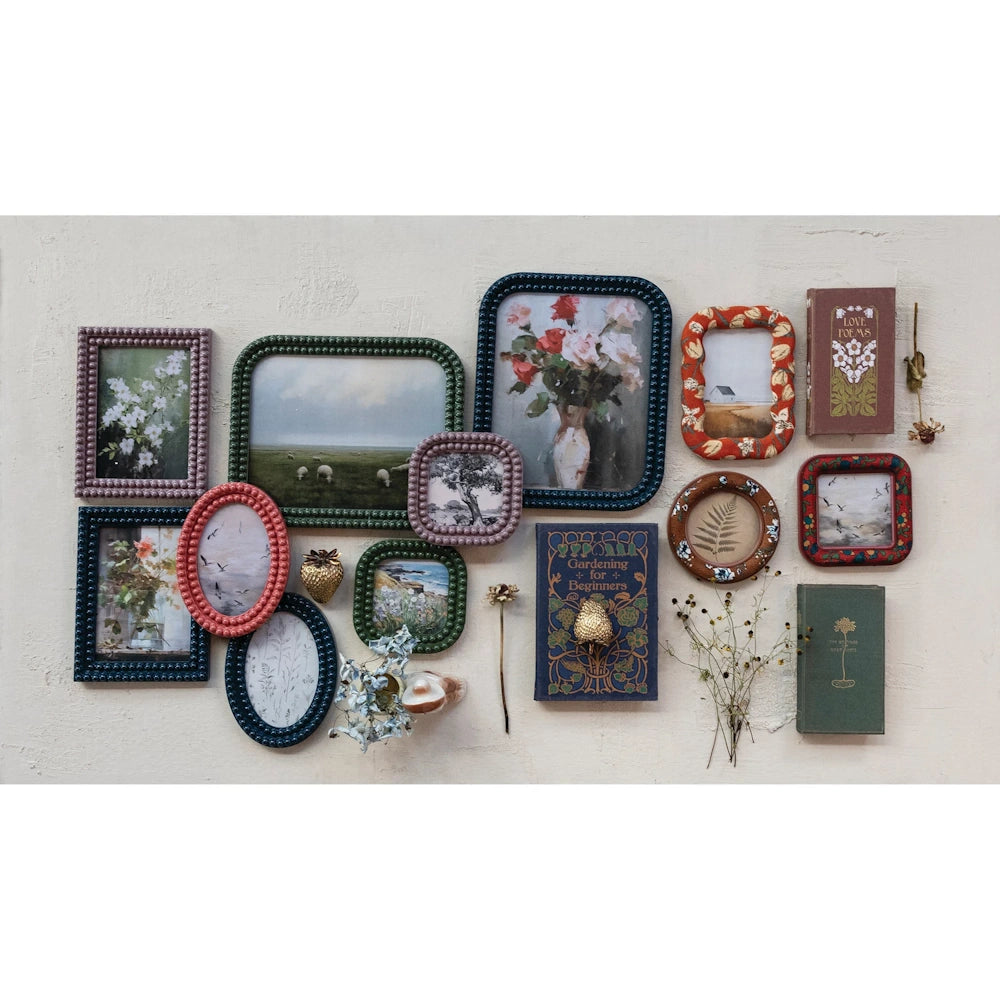 Eclectic gallery wall with colorful bobbin-textured photo frames, vintage art, and old books on a neutral background.