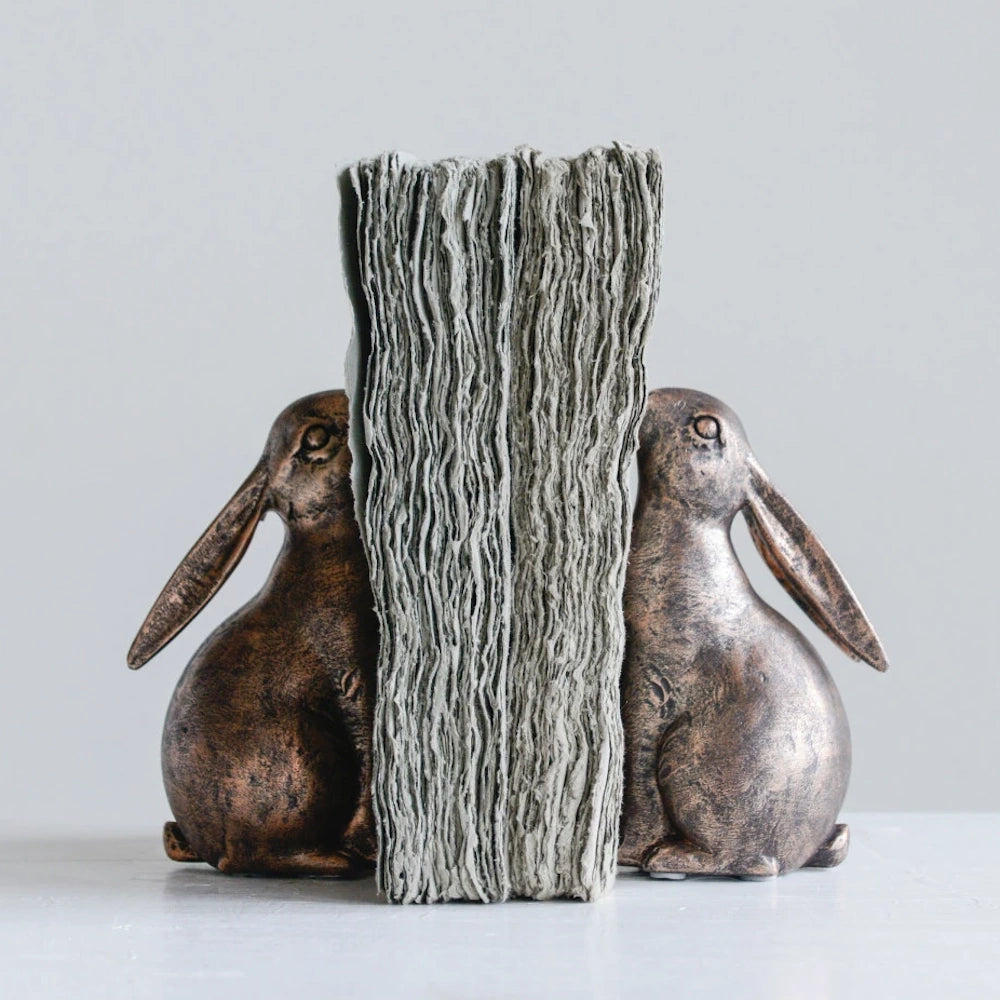 Pair of bronze-finished resin rabbit bookends holding a stack of vintage papers on a white surface.