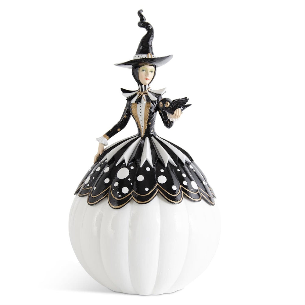 Figurine of a witch in a black and white polka-dot dress, standing on a white pumpkin and holding an owl.