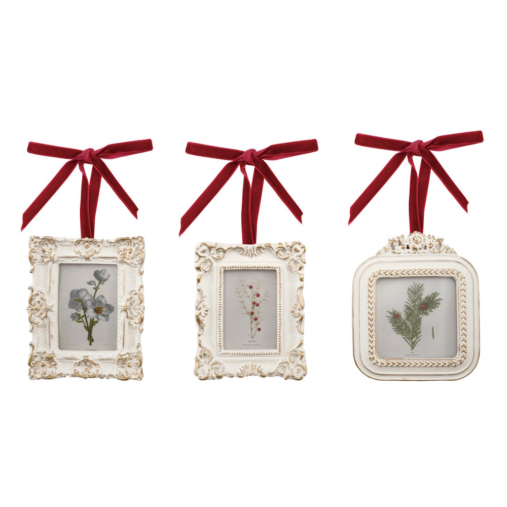 Three ornate vintage white frame ornaments with botanical prints and red velvet hanging bows.