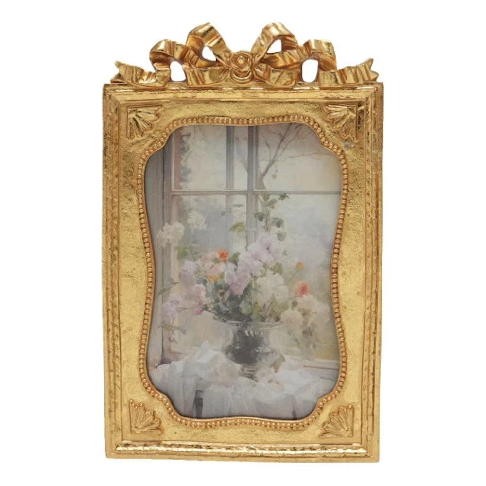 Gold vintage resin photo frame with an ornate ribbon bow top and a floral painting of flowers in a vase.