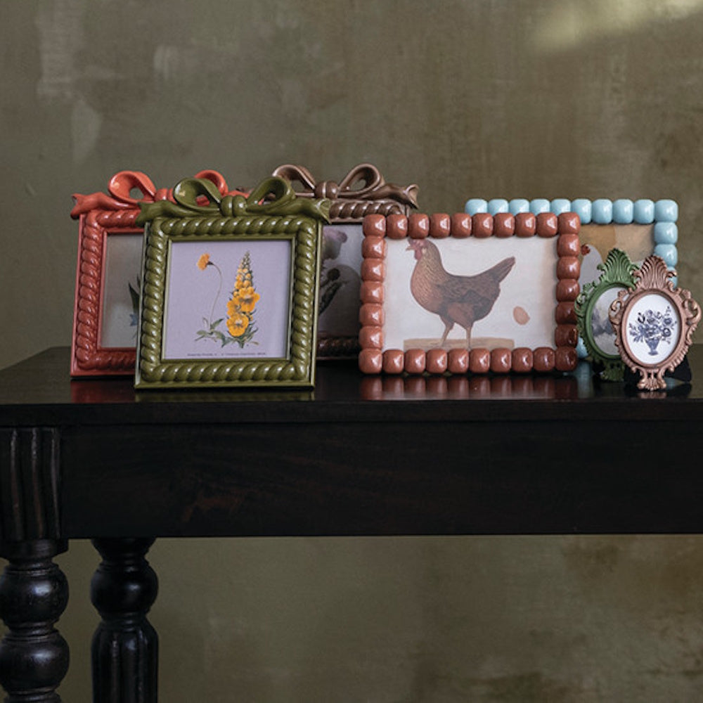 Various resin photo frames displayed on a dark wooden table against a textured wall.
