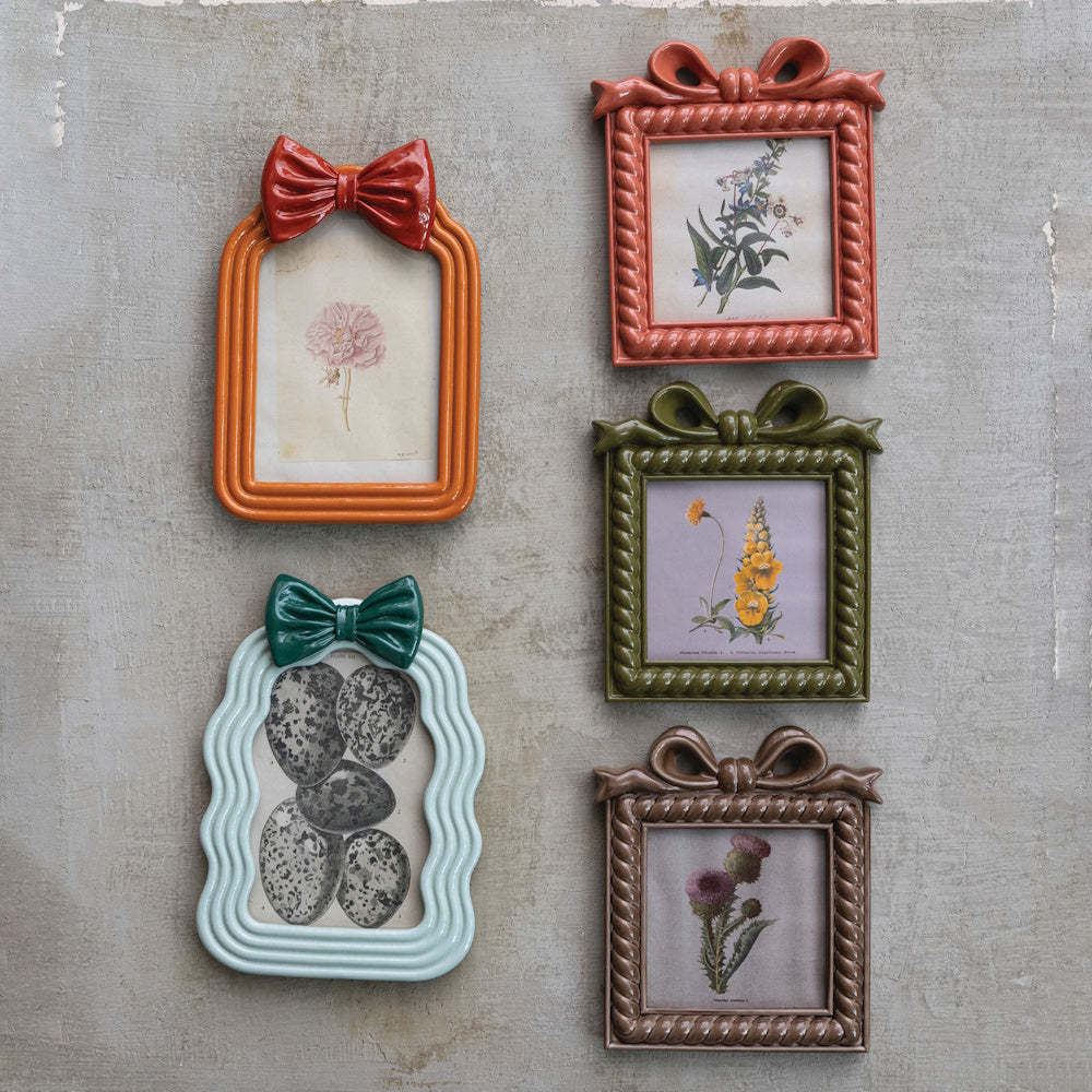 Various resin photo frames with bows and botanical prints hung on a textured wall.