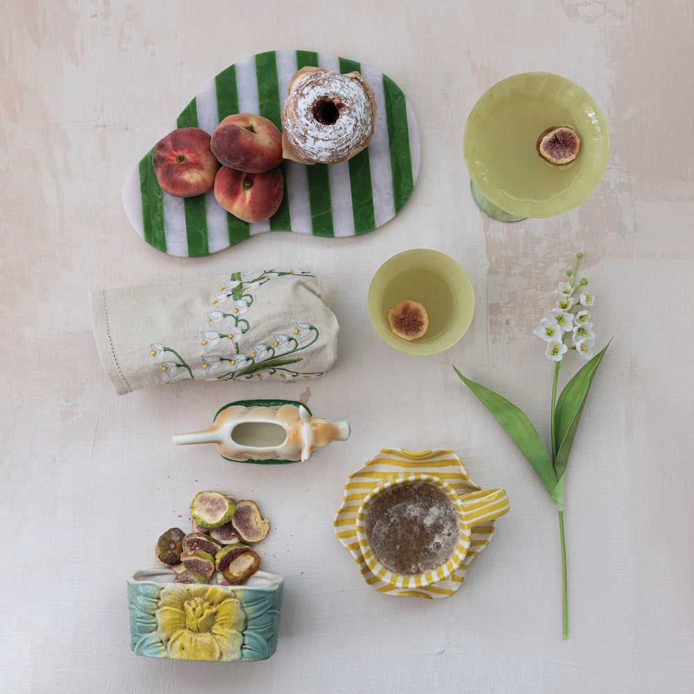 Flat lay of a green striped serving board with peaches, a pastry, coffee, and tableware on a textured surface.
