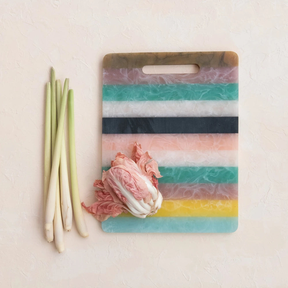 Striped colorful cutting board with fresh lemongrass and radicchio on a neutral textured background.
