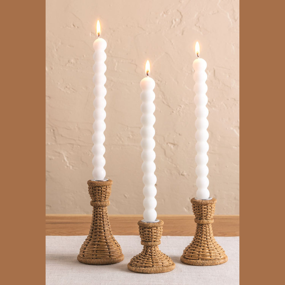 Woven resin taper candle holders with lit white bubble candles on a neutral tabletop, perfect for boho home decor.