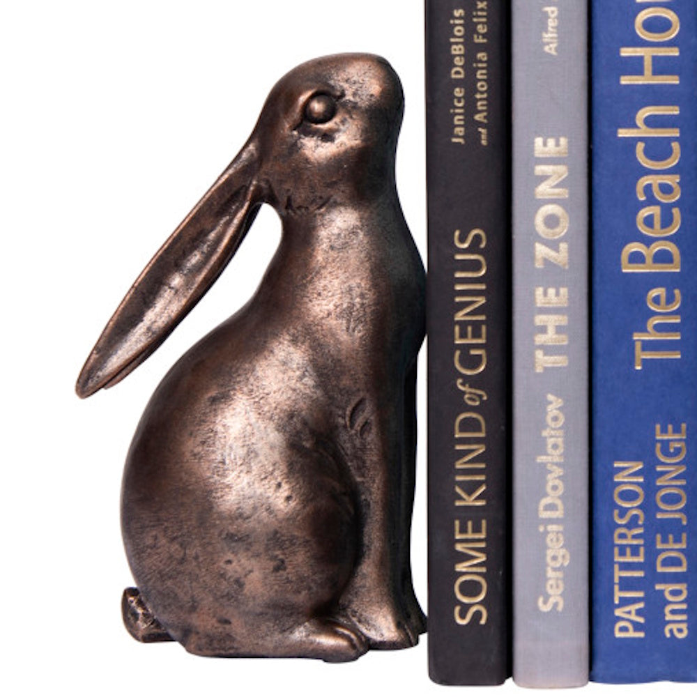 A bronze-colored rabbit sculpture used as a bookend next to three vertical hardcover books.