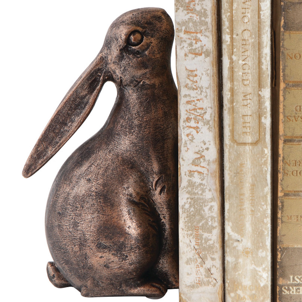 Bronze-colored rabbit bookend holding up vintage books against a white background.