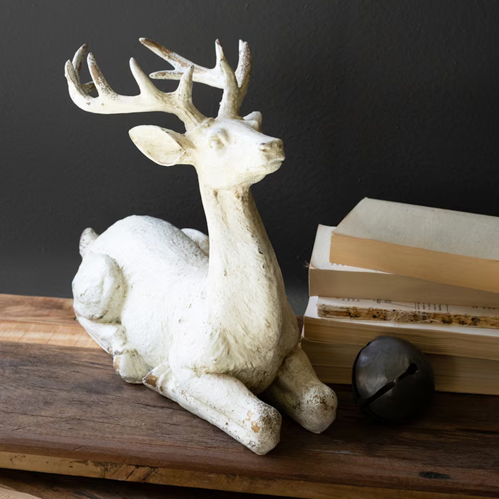 White faux-concrete resting deer figurine next to stacked books on a dark background.