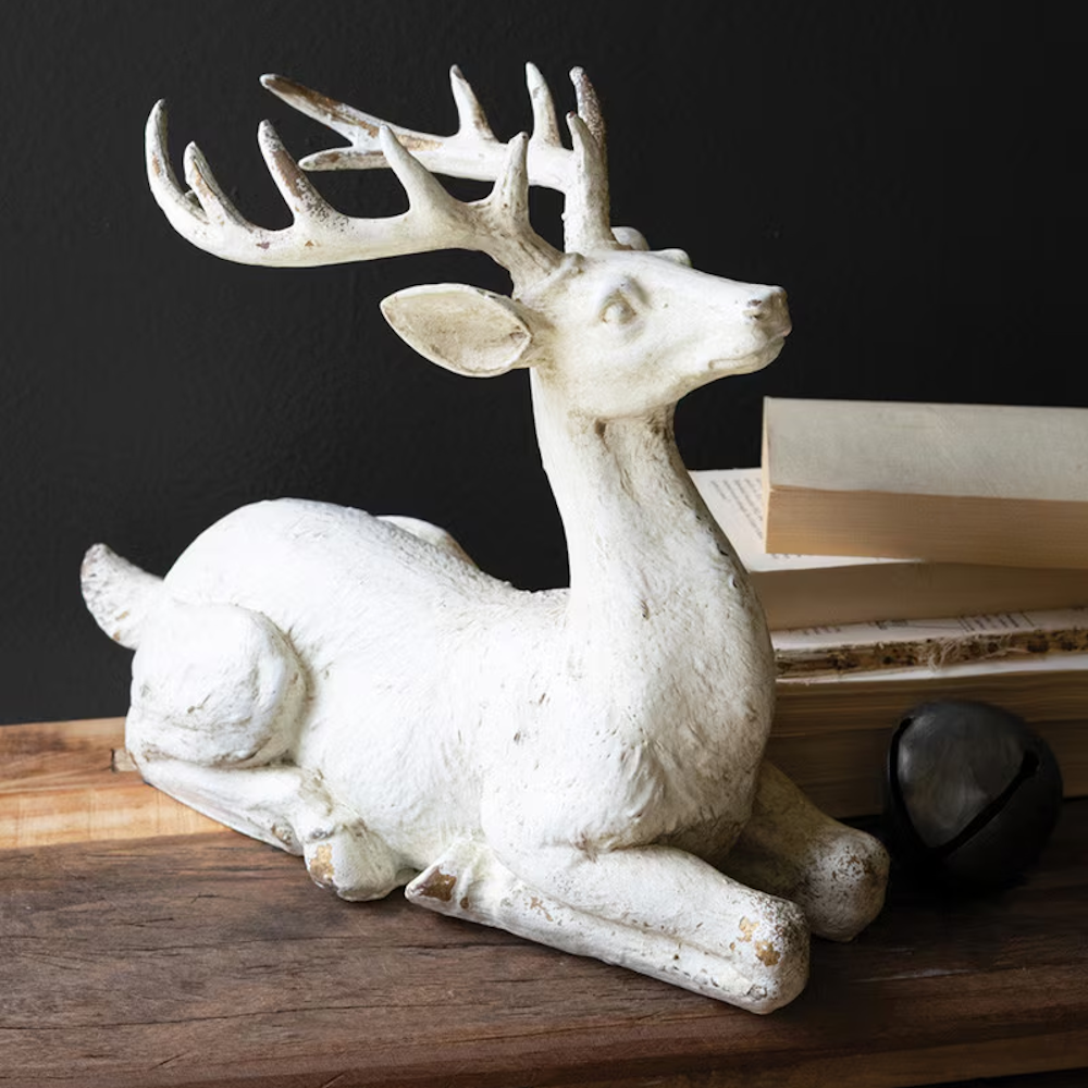 Resting faux-concrete deer figurine with antlers displayed on a rustic wood surface.