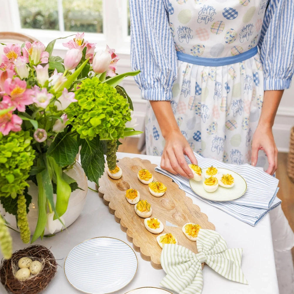 A person serving deviled eggs from a scalloped wooden board decorated with a green bow for an Easter celebration.