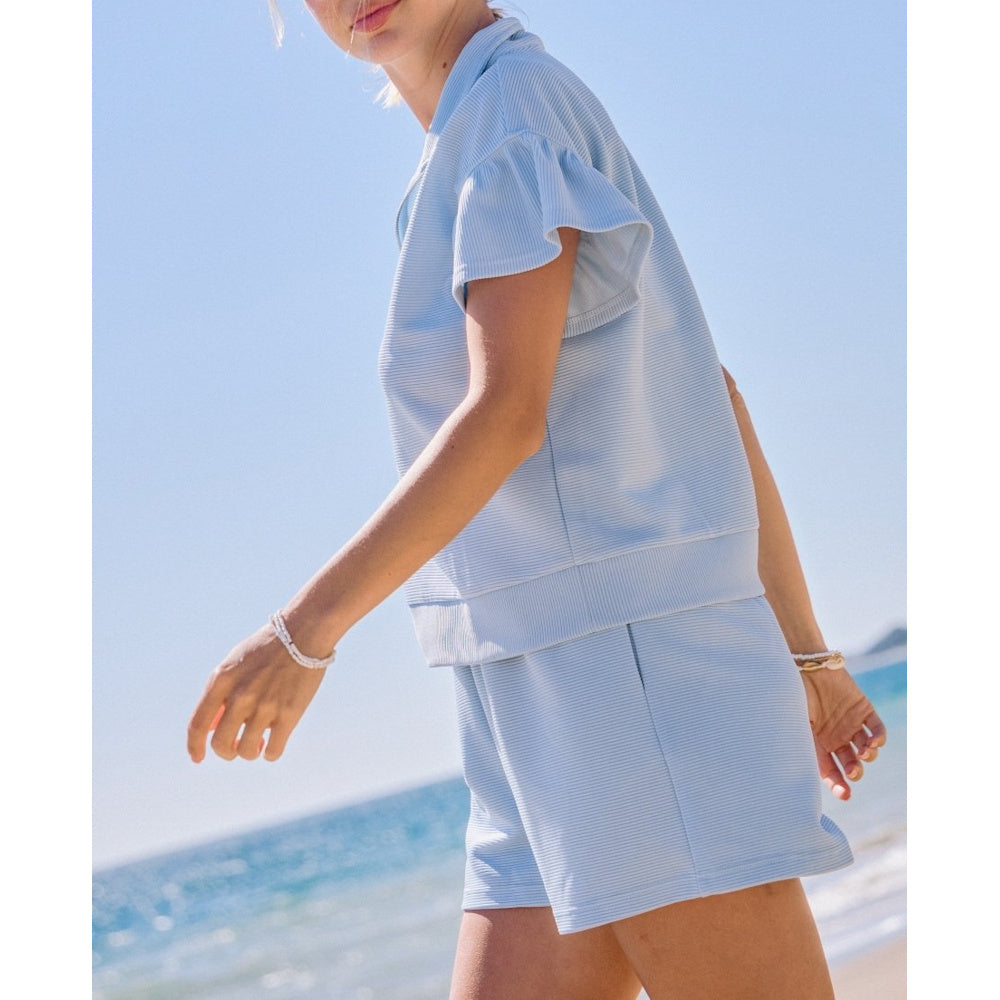 A person walking on a beach wearing a light blue, ribbed short-sleeve top and matching shorts set.