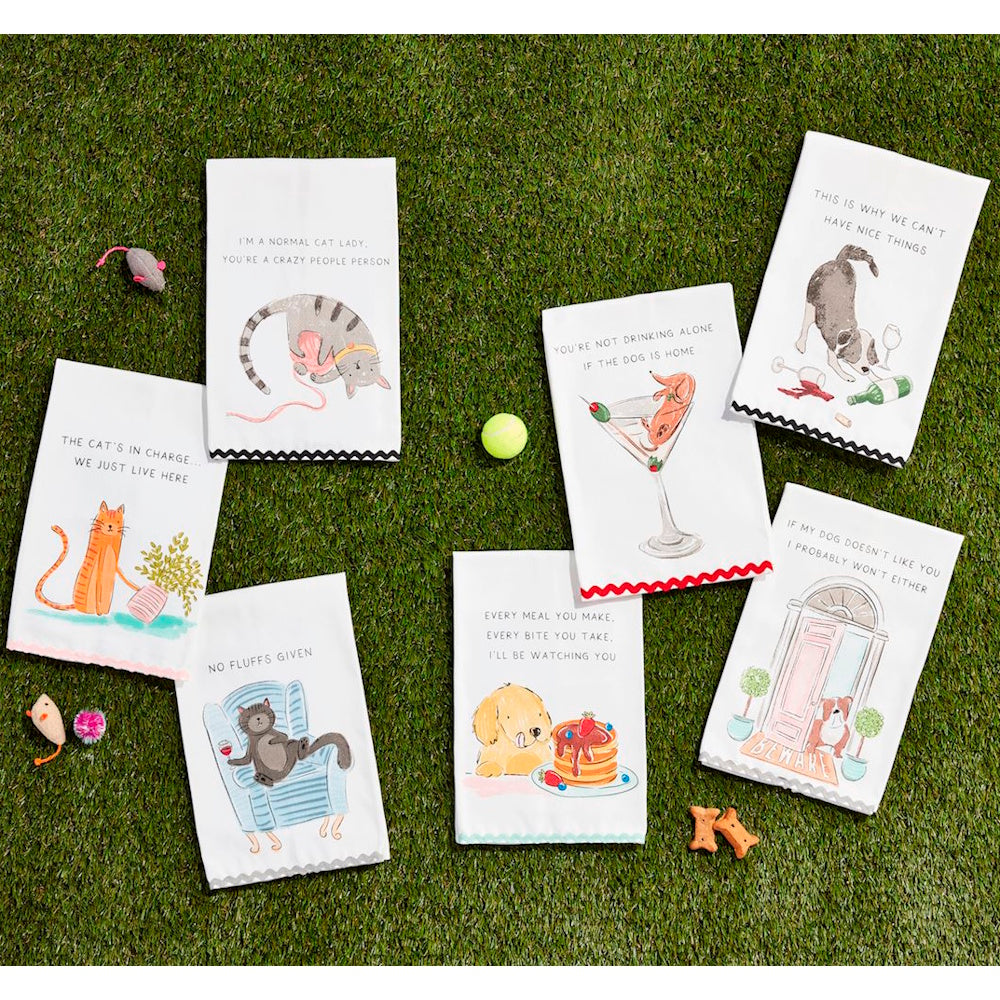 Set of white dishtowels with pet illustrations and funny phrases arranged on grass.
