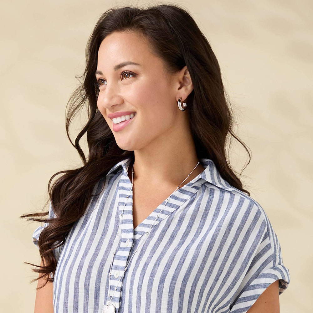 Smiling woman wearing silver stacked hoop earrings and a striped linen shirt.