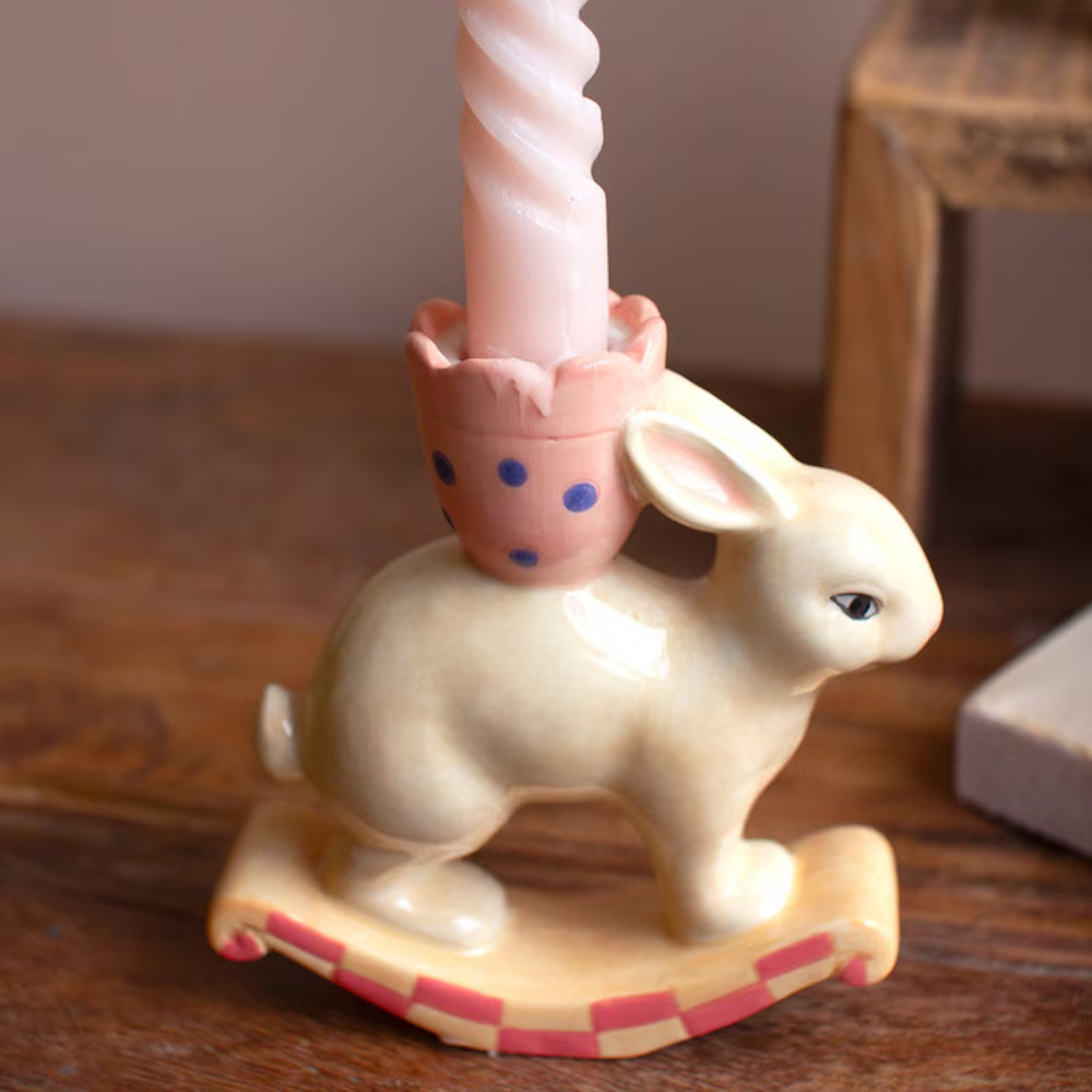 Ceramic rocking bunny taper candle holder with a pink twisted candle on a wooden surface.