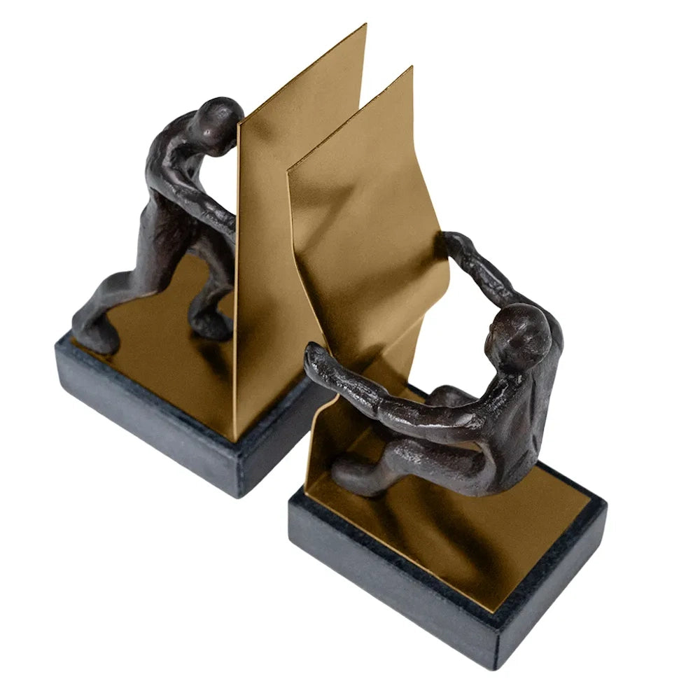 High-angle view of two bronze figures on marble bases pushing and pulling against gold metal bookends.