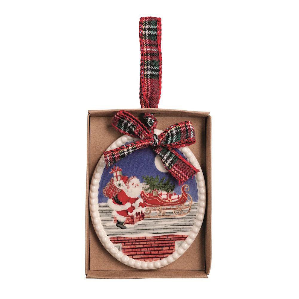 Oval ceramic Christmas ornament depicting Santa on a rooftop with his sleigh, topped with a plaid bow.