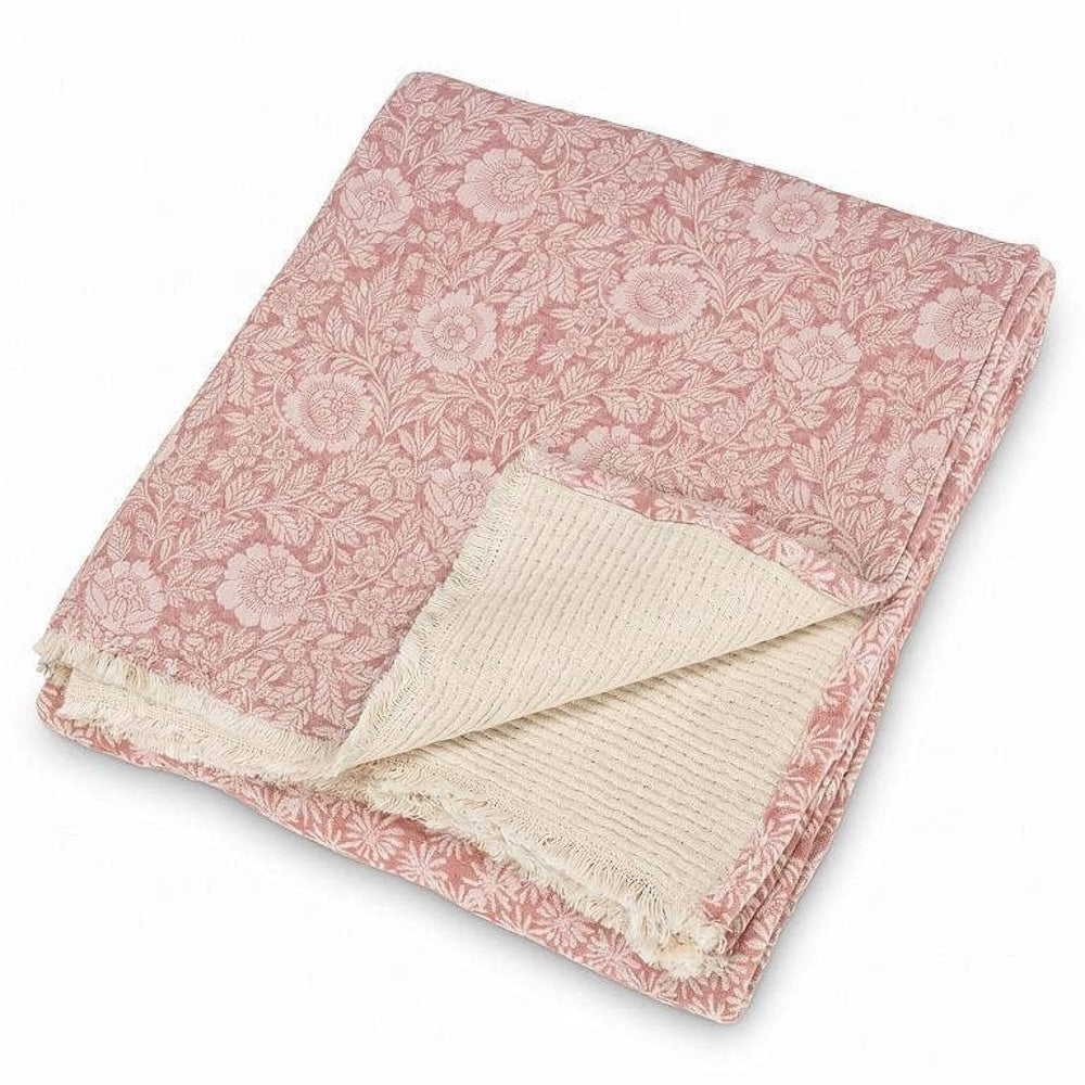 Folded pink and white floral jacquard throw blanket with fringed edges on white background.