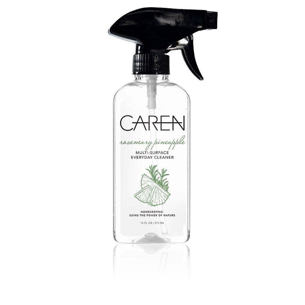 A bottle of CAREN Rosemary Pineapple Multi-Surface Everyday Cleaner in a clear spray bottle with a black nozzle.