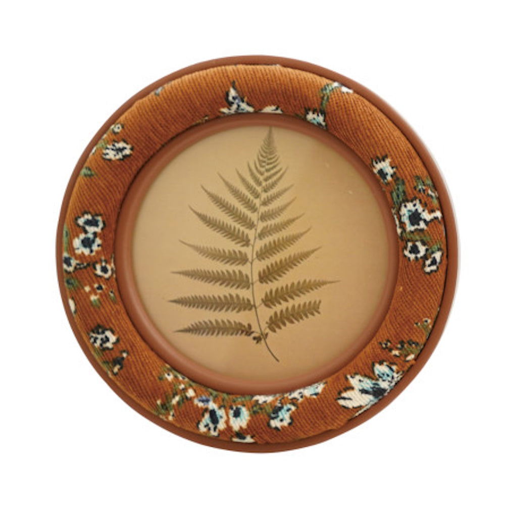 Round frame with an orange floral embroidered border displaying a pressed fern leaf image.