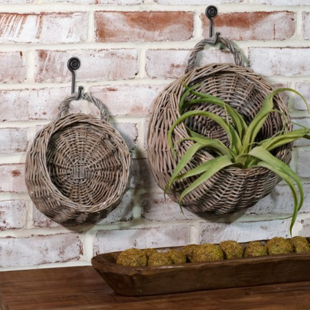 Two round woven willow wall baskets hanging on a brick wall, one filled with green air plants.