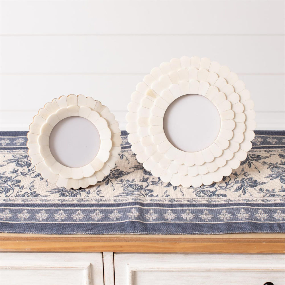 Two round white scalloped bone photo frames in different sizes on a blue and white floral runner.