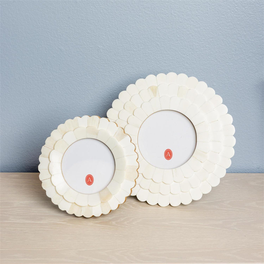 Two round cream scalloped bone picture frames in small and large sizes, displayed on a wooden surface against a blue wall.