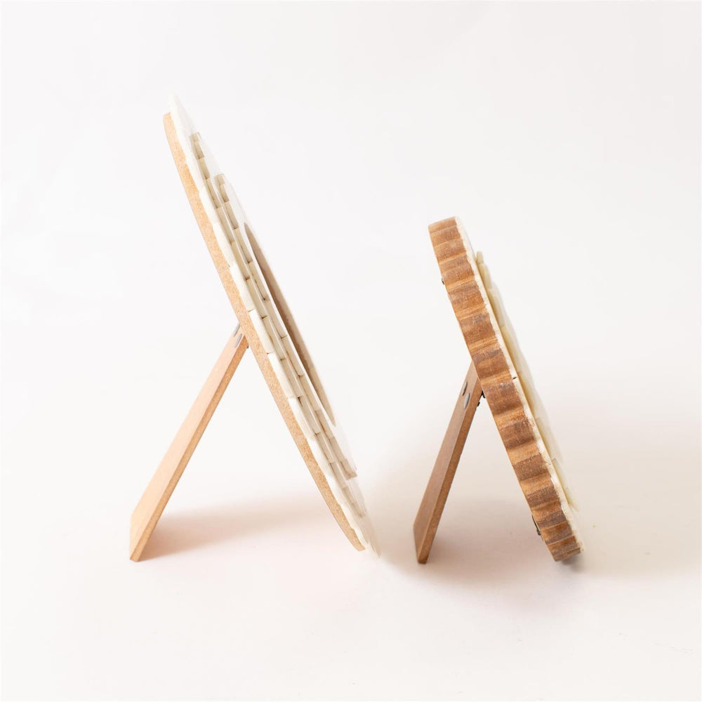 Side view of two round scalloped bone photo frames showing the wooden easel stands and natural wood backing.