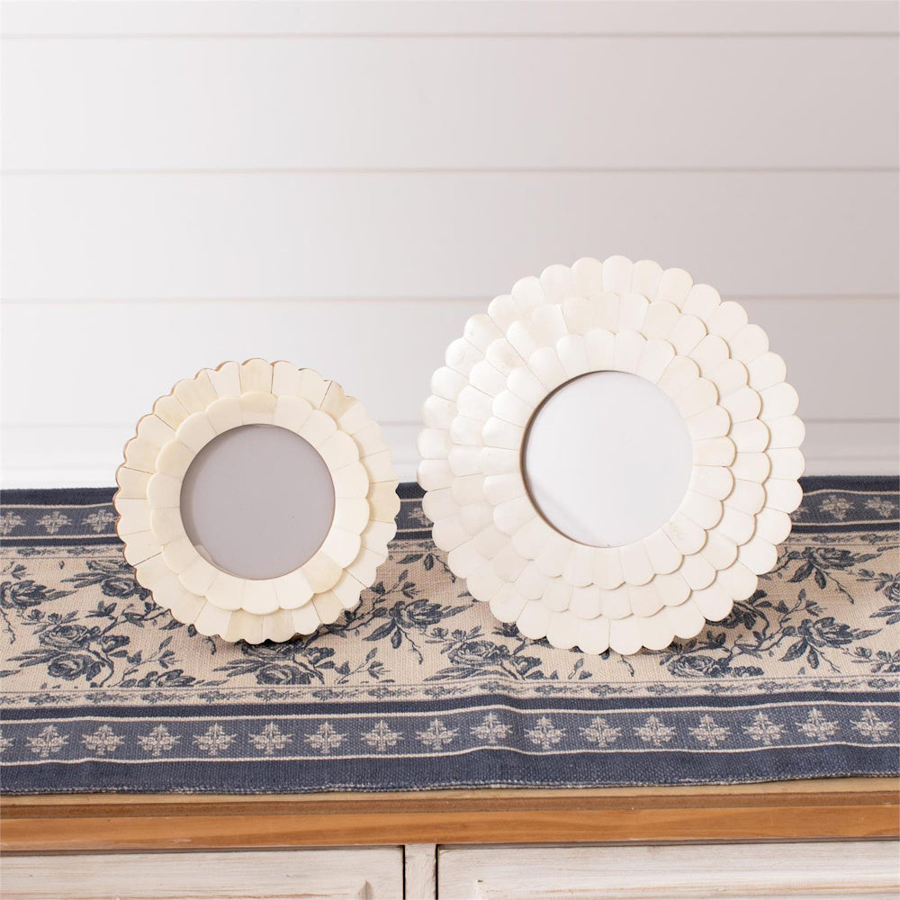 Two round white scalloped bone photo frames in different sizes displayed on a blue and white floral patterned table runner.