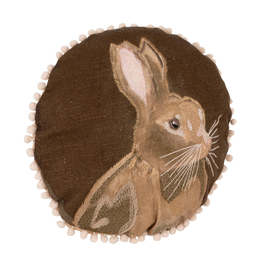 Round brown pillow with an embroidered rabbit and cream pom-pom trim.