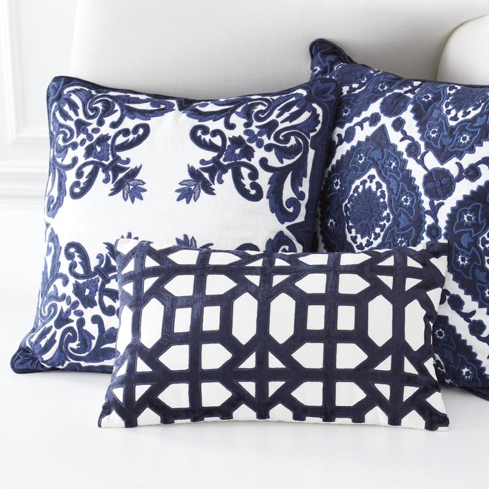 Navy blue and white embroidered decorative pillows with geometric and floral patterns on a white sofa.