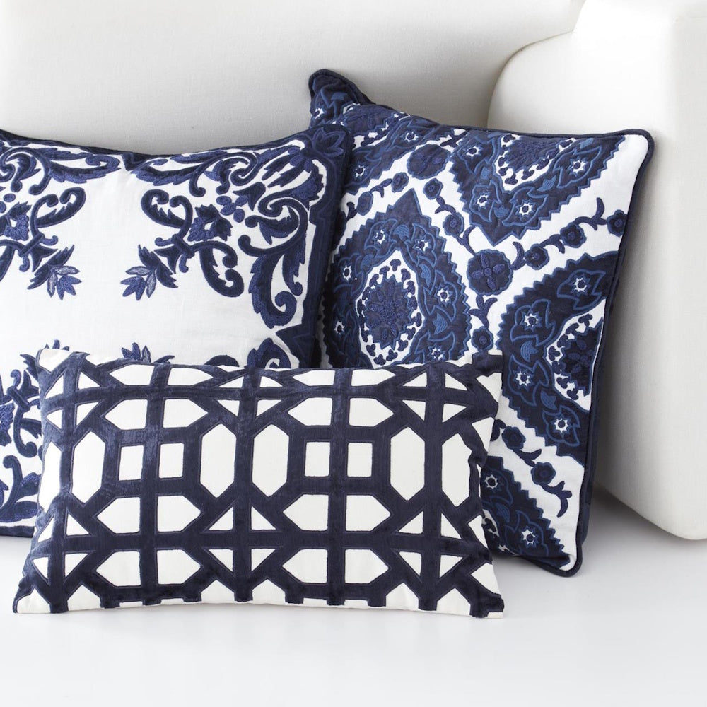 Decorative navy blue and white embroidered throw pillows with geometric and floral patterns on a white sofa.