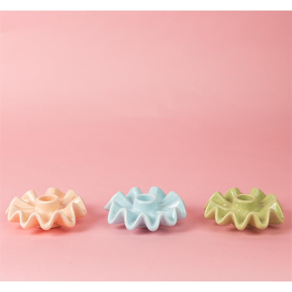 Three pastel ceramic ruffle taper candle holders in pink, blue, and green on a pink background.