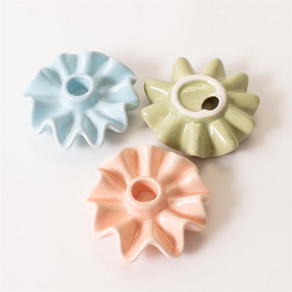 Three pastel ceramic ruffled candle holders in blue, green, and pink on a white surface.