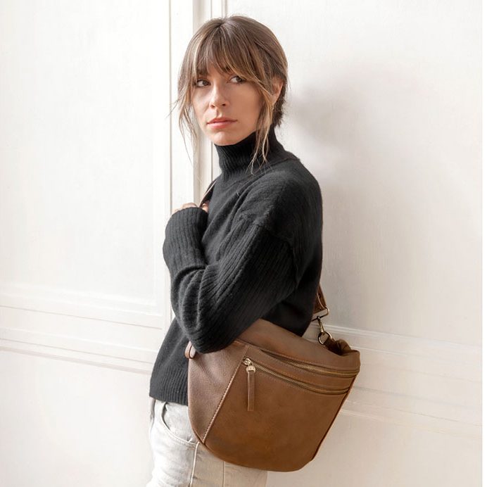 Woman wearing a russet brown leather large sling crossbody bag over a black turtleneck sweater.