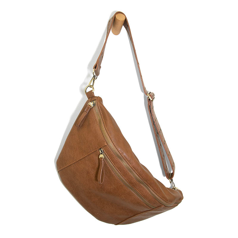 Russet brown faux leather crescent sling bag with gold zippers and an adjustable strap hanging on a wooden wall peg.