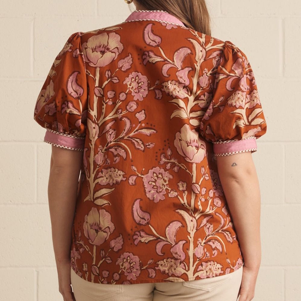 Back view of a rust-colored top with pink floral print, cuffed puff sleeves, and pink patterned trim.