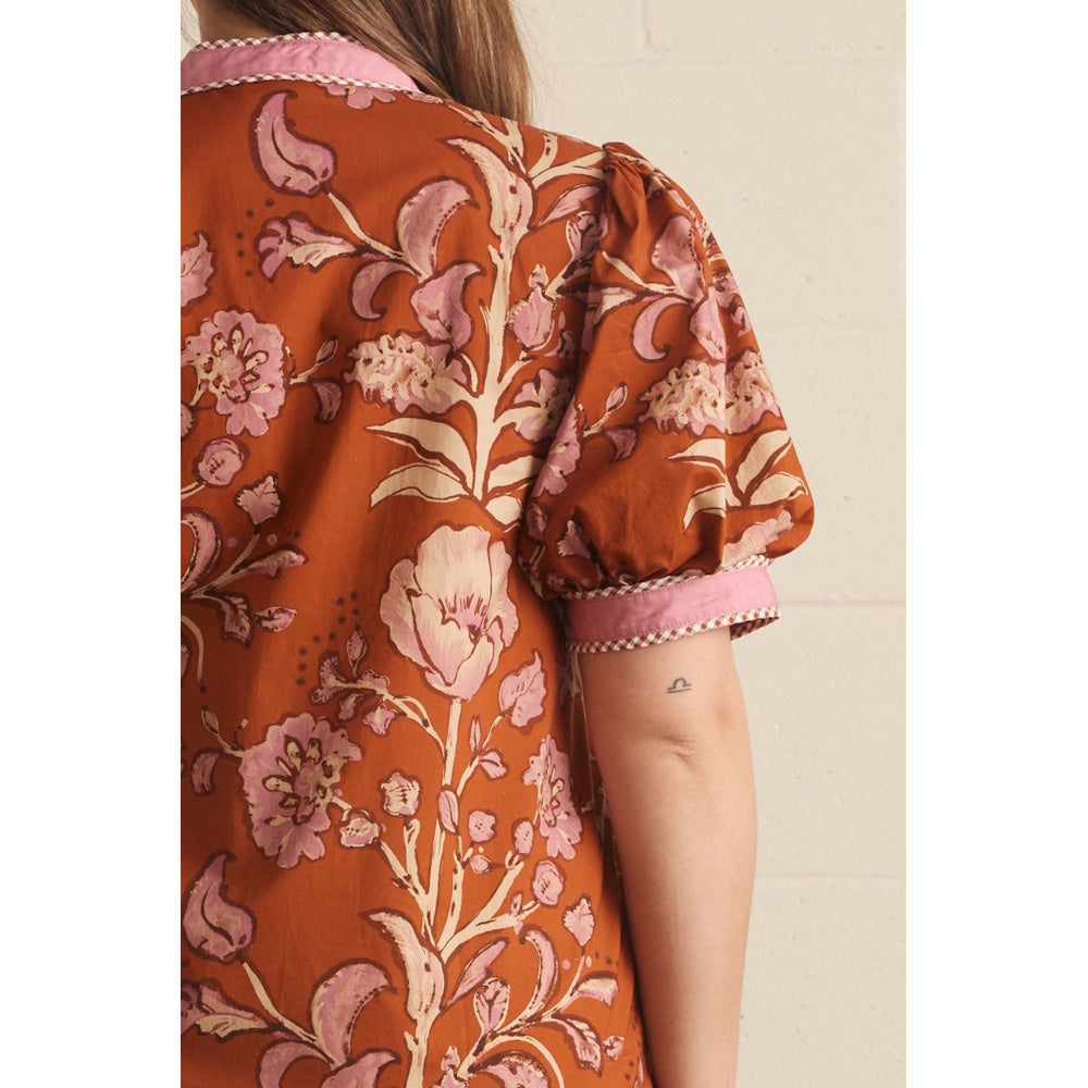 Close-up back view of a rust floral top showing puff sleeve detail and pink checked trim.