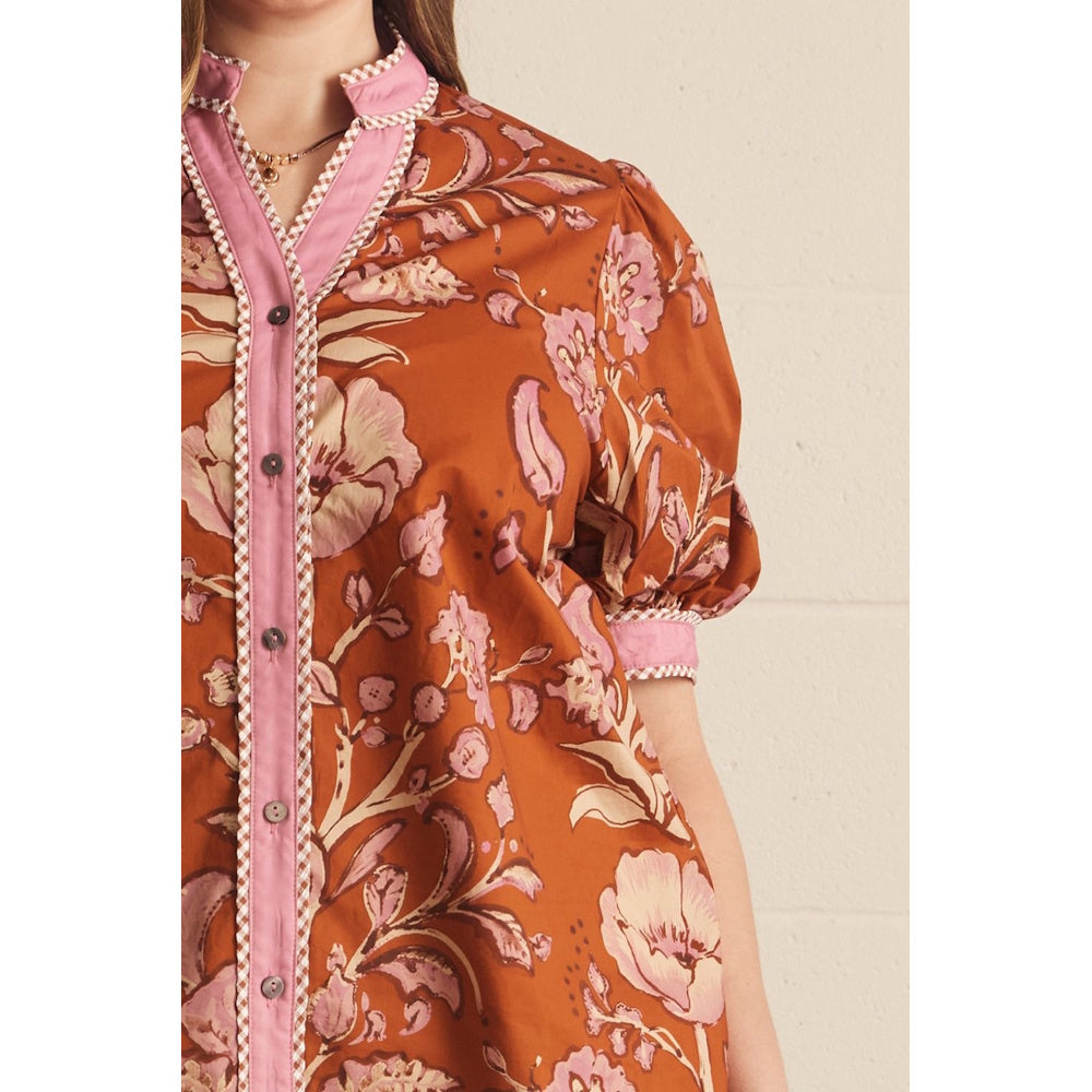 Close-up of a rust floral print top featuring a pink button placket and checkered piping trim.