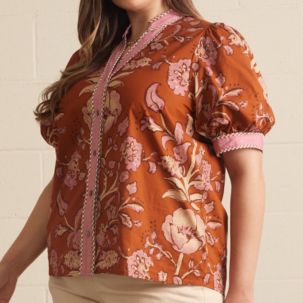 Three-quarter view of a rust floral print top featuring a pink button placket and puff sleeve.