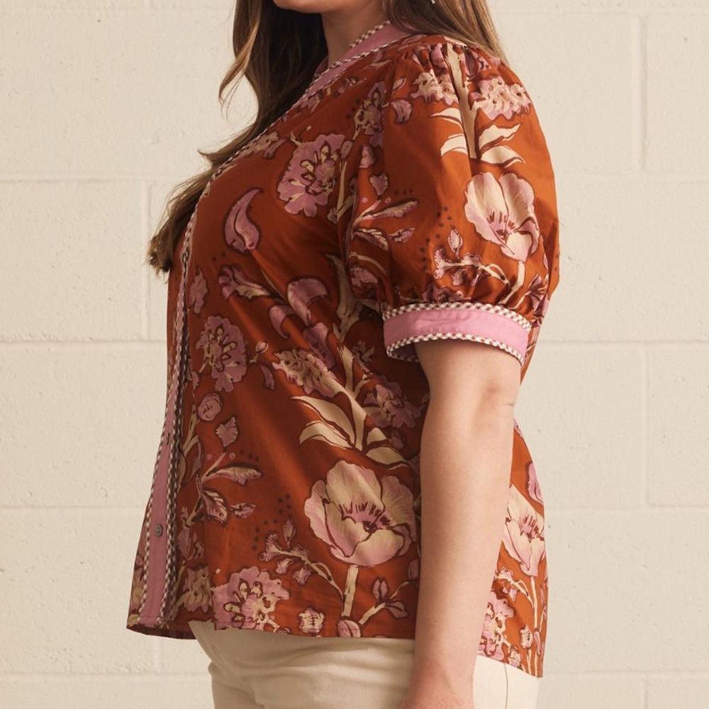 Side profile of a rust-colored top featuring pink floral print and contrasting pink sleeve cuffs.