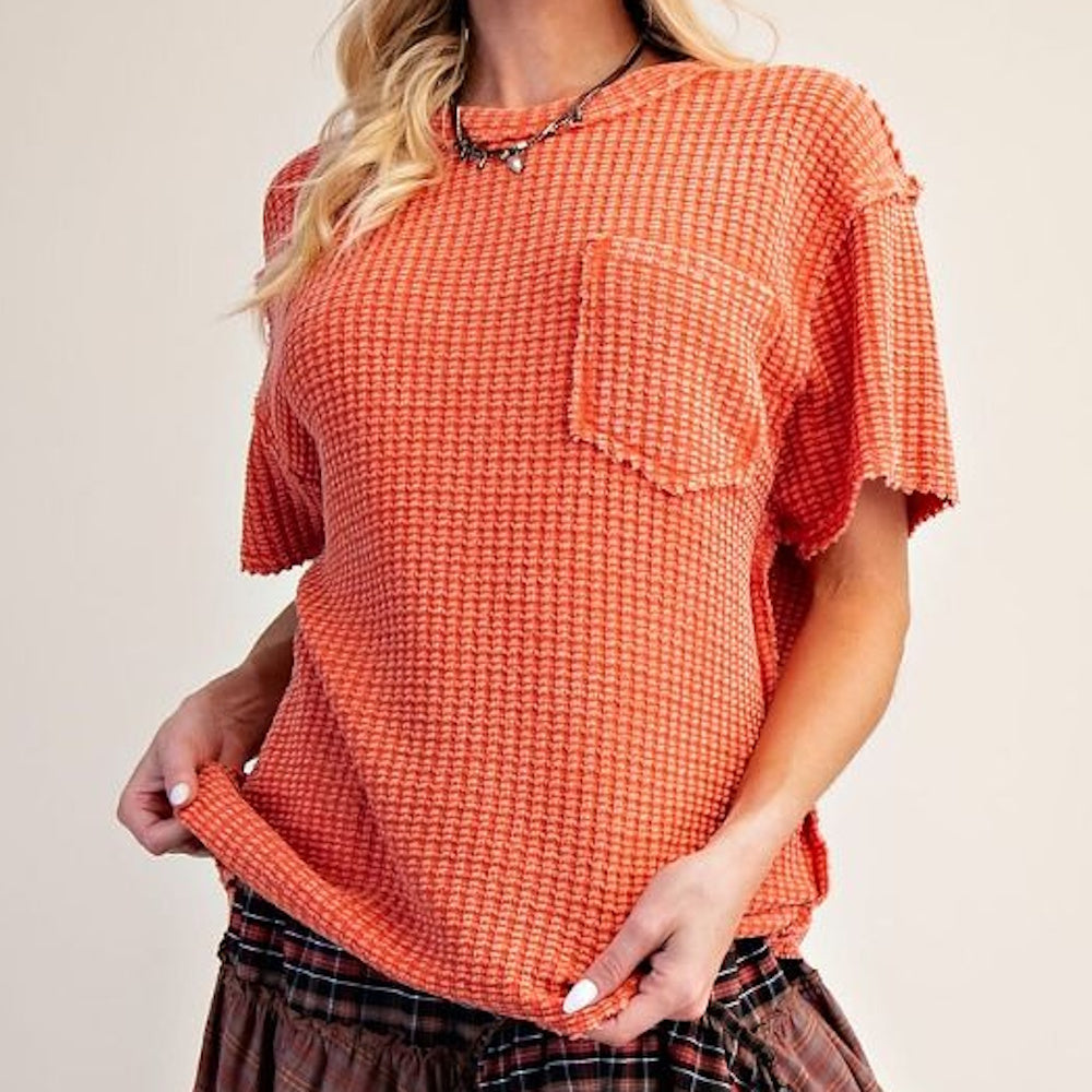 Front view of a rust orange waffle knit short-sleeve top with a chest pocket and raw edge seams.