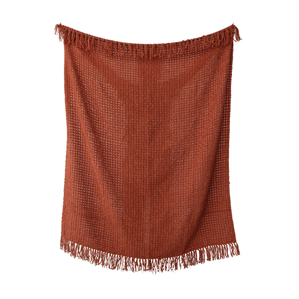 Rust-orange waffle weave throw blanket with fringed edges hanging against a white background.